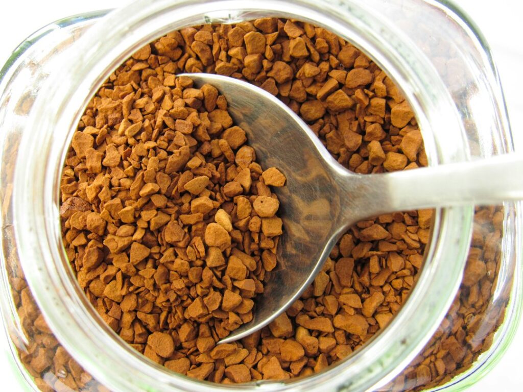 Spoon scooping instant coffee granules from glass jar