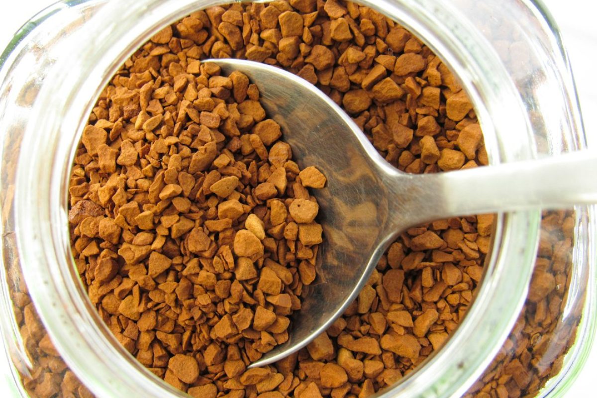Spoon scooping instant coffee granules from glass jar